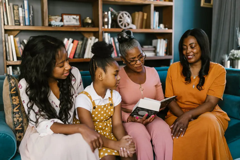 Three generations of a family reading together on a sofa, in front of a home bookshelf.
