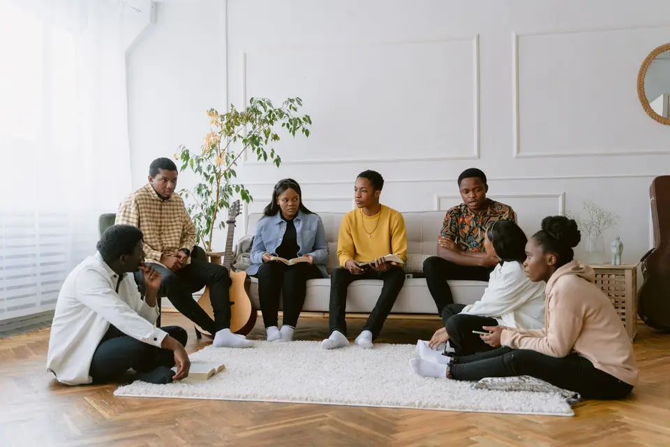 A small group of adults sitting together in a bright living room, talking.